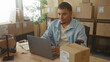 © Krakenimages.com - Man typing on laptop in building among stacked boxes and packaging at a small business desk; entrepreneurship pride.