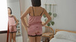 © Krakenimages.com - Woman posing with hands on hips in pink pajamas beside a mirror in a sunlit bedroom; intimate confidence.