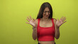 © Krakenimages.com - Young woman in studio with palms out and hands raised against lime green backdrop, squinting repulsed face wearing red crop top; disgust hesitation avoidance.
