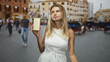 © Krakenimages.com - Woman holding white chocolate bar with bare forearm visible, holds bar up while standing on street piazza with historic buildings and carriages; temptation craving.