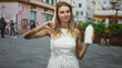 © Krakenimages.com - Blonde woman holding a glass milk bottle while giving a thumbs down gesture on a pedestrian street with cafes and planters; disapproval critique.