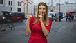 © Krakenimages.com - Woman in red shirt points thumb and holds finger to lips for silence on street; playful secrecy.
