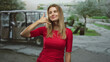 © Krakenimages.com - Woman in red shirt making phone hand gesture with her right hand near face, smiling while standing on a street beside a parked golf cart and paved path; playful invitation.