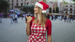 © Krakenimages.com - Blonde woman cook wearing red gingham apron and santa hat gives thumbs up while standing in a busy street plaza; holiday cheer.