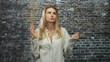 © Krakenimages.com - Blonde woman in striped shirt holds pinched fingers and a clenched fist while closing eyes and pursing lips in a studio brick wall setting; serene contemplation.
