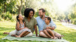 © Xenia - Happy mixed race family laughing together on a picnic blanket in the park. Diverse parents and two children enjoying a sunny summer day outdoors. Family bonding and leisure concept
