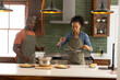 © wavebreak3 - Diverse couple wearing gray aprons preparing pasta at white countertop island, plating two dishes