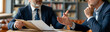© pattozher - Strategic Discussion: Two businessmen in sharp suits engage in a focused discussion over documents, possibly in a modern office or co-working space, highlighting collaboration and decision-making.
