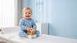 © Anastasiia Guva - Smiling blonde toddler sitting on examination table in pediatric clinic playing with wooden ABC block, happy child healthcare and medical checkup concept with copy space