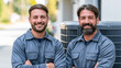 © Olga Ко - Retrato de dos técnicos profesionales de HVAC sonriendo junto a una unidad de aire acondicionado exterior