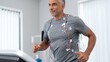 © ЮРИЙ ПОЗДНИКОВ - Middle-aged man running on treadmill with medical monitoring equipment in fitness center
