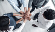 © Okw - Team joining hands together in a circle on a bright office floor, symbolizing unity, cooperation, and teamwork, success and partnership