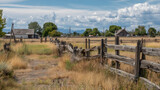 Abandoned rural homestead with dry grass and weathered wooden fences under cloudy sky creating nostalgic countryside atmosphere and isolation mood