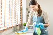 © KMPZZZ - Cleanliness, asian young woman work chore cleaning on cupboard at home, hand wearing glove using wiping cloth remove dust with spray bottle. Household hygiene clean up, equipment tool for cleaning
