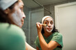 © Marko Geber - Young woman applying facial mask with brush in bathroom mirror