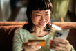 © Davor - Smiling woman shopping online with credit card on smartphone at home