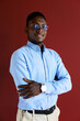 © MiniDiem - Confident black businessman standing with crossed arms, smiling at camera, wearing glasses and a light blue shirt, representing professionalism and success in a corporate environment