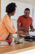 © wavebreak3 - African American couple cooking together in kitchen, making salad bowl with cucumber and frying pan