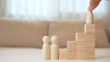 © Punyawee - A hand moves a wooden child figure up block steps to the top, beside parent figures, representing growth, encouragement, achievement, parental support, guidance, aspiration, and family success.