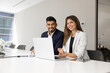 © fizkes - Portrait of two happy multinational colleagues, Hispanic and Indian team members smiling at camera sit at modern office desk with laptop. Teamwork, diversity, leadership, positive corporate workflow