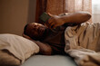 © Seventyfour - Black young adult man lying in bed, squinting at smartphone and covering head, showing screen fatigue and digital addiction at home. For sleep health, tech overuse, wellness campaigns