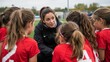 © olga_demina - A female sport trainer gives instructions to a group of young girls in red soccer jerseys on a green field.