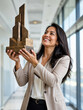 © SerPak - A woman in a beige blazer joyfully holds a trophy in a modern office setting. Professional success and recognition.