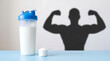 © MUHAMMAD - Protein shaker cup with scoop powder and a shadow of a muscular bodybuilder athlete