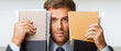 © Kingdola - Holding Files: A businessman in a suit stands holding two file folders in front of his face, looking directly at the camera with a serious expression.