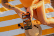 © mary_markevich - top view from above on woman hands holding using smartphone sitting on beach on summer season vacation wearing yellow swimsuit, bright colorful