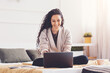 © Prostock-studio - Smiling Middle Eastern Woman In Casual Outfit Working On Laptop While Sitting Cross-legged On Bed At Home, Joyful And Focused In Cozy Living Space. Remote Work Concept