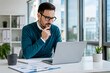 © Abdelati - Focused Businessman Working on Laptop in Modern Office with Window View