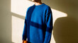 © Rendara Studio - Introspective person stands in blue sweater with window shadow on cream wall