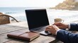 © MT - Professional businessman working remotely on laptop at outdoor seaside cafe table with coffee and notebook representing digital nomad executive lifestyle