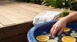 © Nina - Hand in Ice Water Bowl with Citrus Fruit Slices for Cold Plunge Recovery Therapy and Refreshing Spa Treatment Outdoors on Wooden Deck