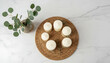 © tae - Overhead view of elegant white candles on woven rattan tray beside ceramic vase holding fresh eucalyptus leaves over luxury marble background surface with empty copy space for text