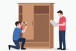 © Himel - Two men work together to assemble a large wooden wardrobe, with one using tools and the other reading the instruction manual.
