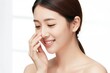© Pete - Young Asian woman smiles gently touching her nose. Her clear, healthy skin radiates freshness. She appears cheerful and content with natural beauty.
