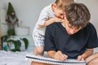 ©  Tsvyk L. - Older brother drawing in sketchbook while little brother looks over his shoulder at home