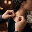 © Agus - A romantic moment of a partner carefully fastening a delicate gold necklace around a woman's neck in an intimate evening setting