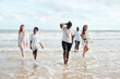 © offsuperphoto - A diverse group of six people walking in the shallow ocean waves on a sandy beach. They are dressed in casual summer attire