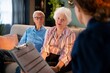 © Videophilia - An older couple sits on a couch in a cozy living room. They are having a discussion with a person holding a clipboard. The room is bright and has plants and a clock on the wall.