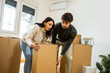 © Mediteraneo - A happy young couple lifting cardboard boxes together during relocation in a new apartment