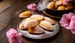 © Karina - sweet delectable madeleines dusting of powdered sugar rustic wooden table and delicate pink flowers