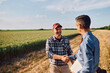 © Drazen - Happy mature farmer shaking hands with investment consultant in field.