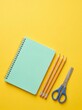 © AdPremium - Mint Green Spiral Notebook with Three Pencils and Blue Scissors on Yellow Background