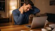 © Djemari - A man experiencing neck pain and stress while working on his laptop late at night at home.