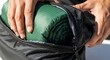 © Lucas - Closeup of a person packing a green camping sleeping bag into a black compression sack for travel or outdoor adventure