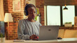 © DC Studio - Teleworker listening to music and solving daily tasks, self employed woman. African American girl having fun with headset while she works on duties during sunset hour at home. Handheld shot.