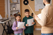 © Pixel-Shot - Children learning music with teacher, young students practicing singing with sheet music and conductor, children are actively engaged in a music lesson with their teacher